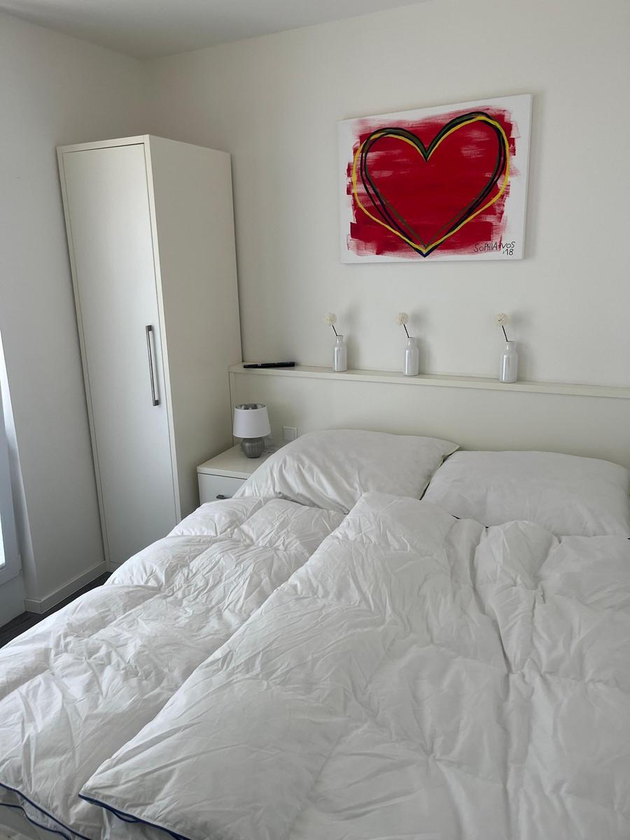 Schlafzimmer mit weißem Bett, Kleiderschrank und Wandbild mit Herz.