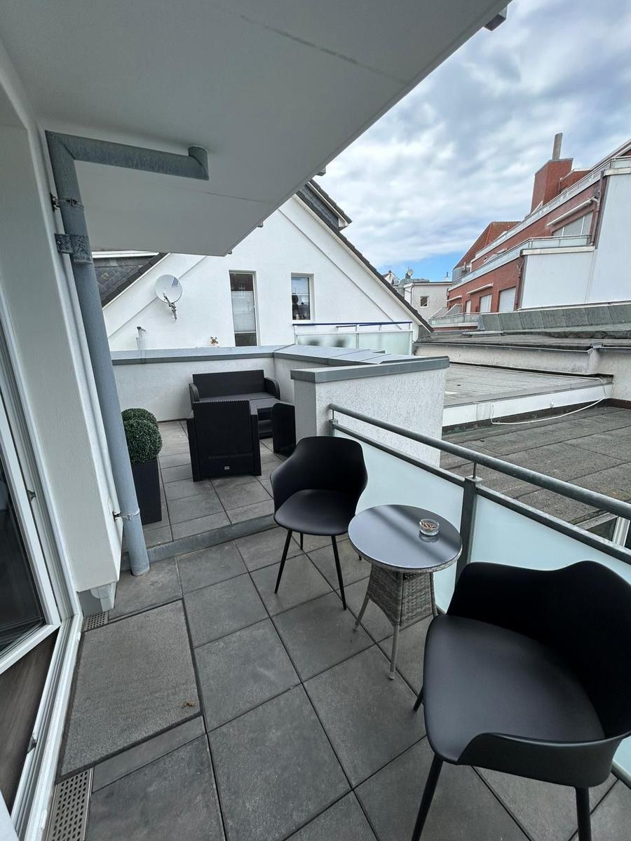 Terrasse mit Sitzgruppe, Tisch und Pflanze. Blick auf Dächer und Gebäude.