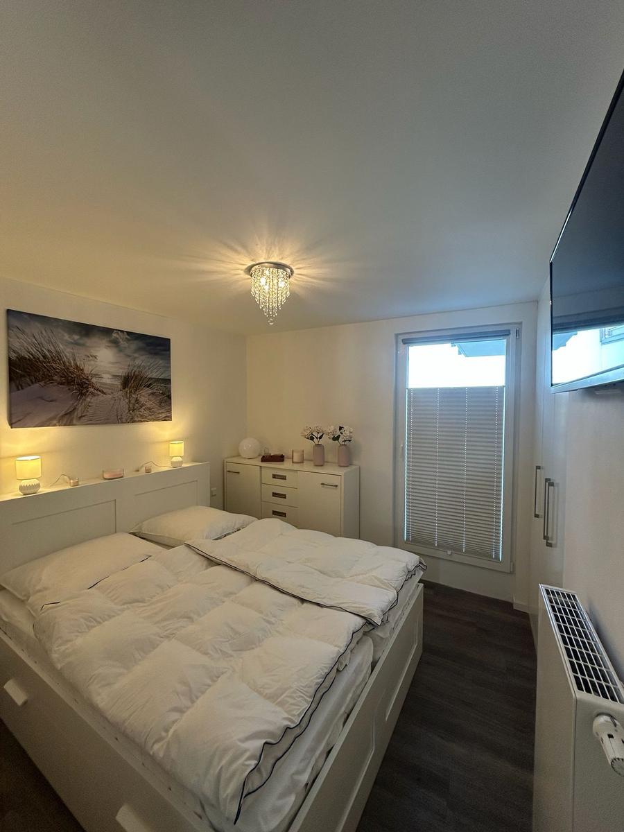 Schlafzimmer mit Doppelbett, Schrank, Fenster und Deckenleuchte.