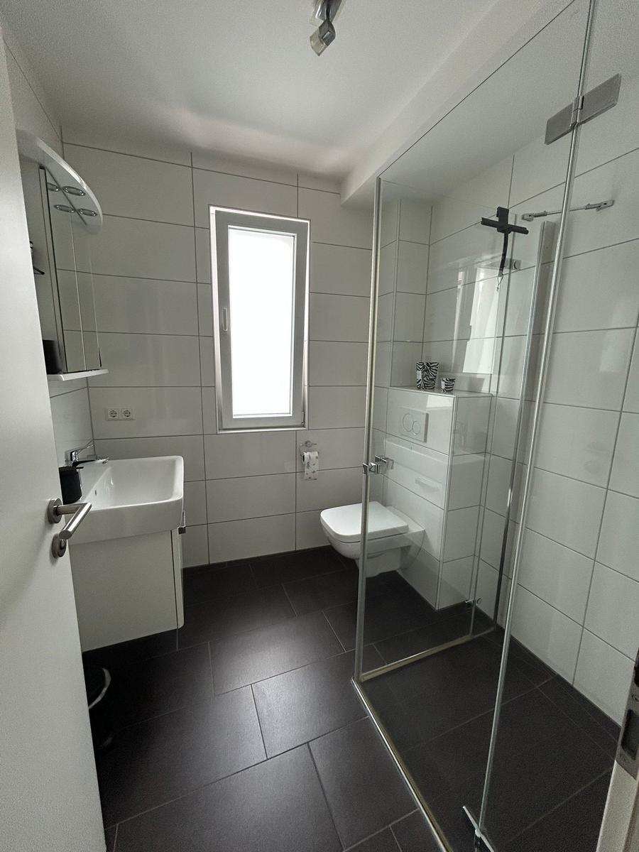 Badezimmer mit Dusche, WC und Waschbecken. Weiße Fliesen und dunkle Bodenfliesen.