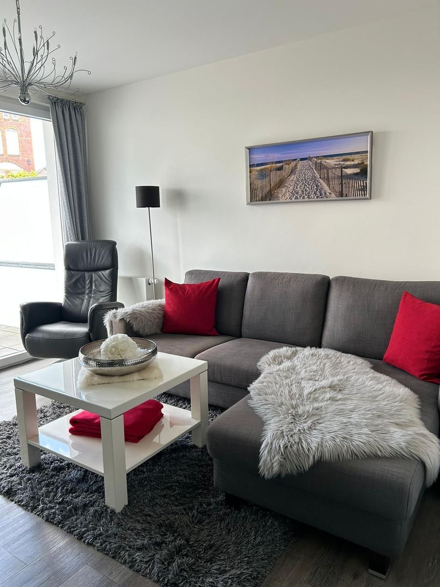 Ein Wohnzimmer mit grauem Sofa, roten Kissen und einem weißen Couchtisch.