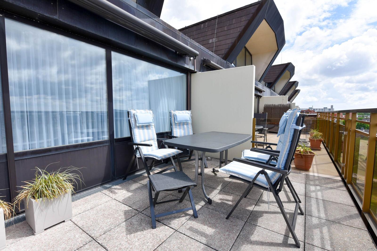 Terrasse mit Tisch und vier Stühlen, Pflanzen und Blick auf Gebäude.