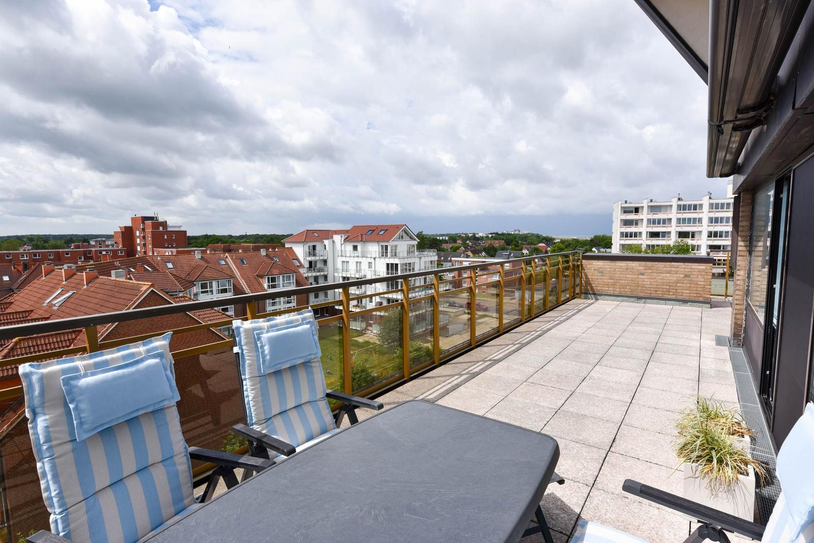 Terrasse mit Liegestühlen und Tisch. Blick auf Wohnhäuser und Himmel.