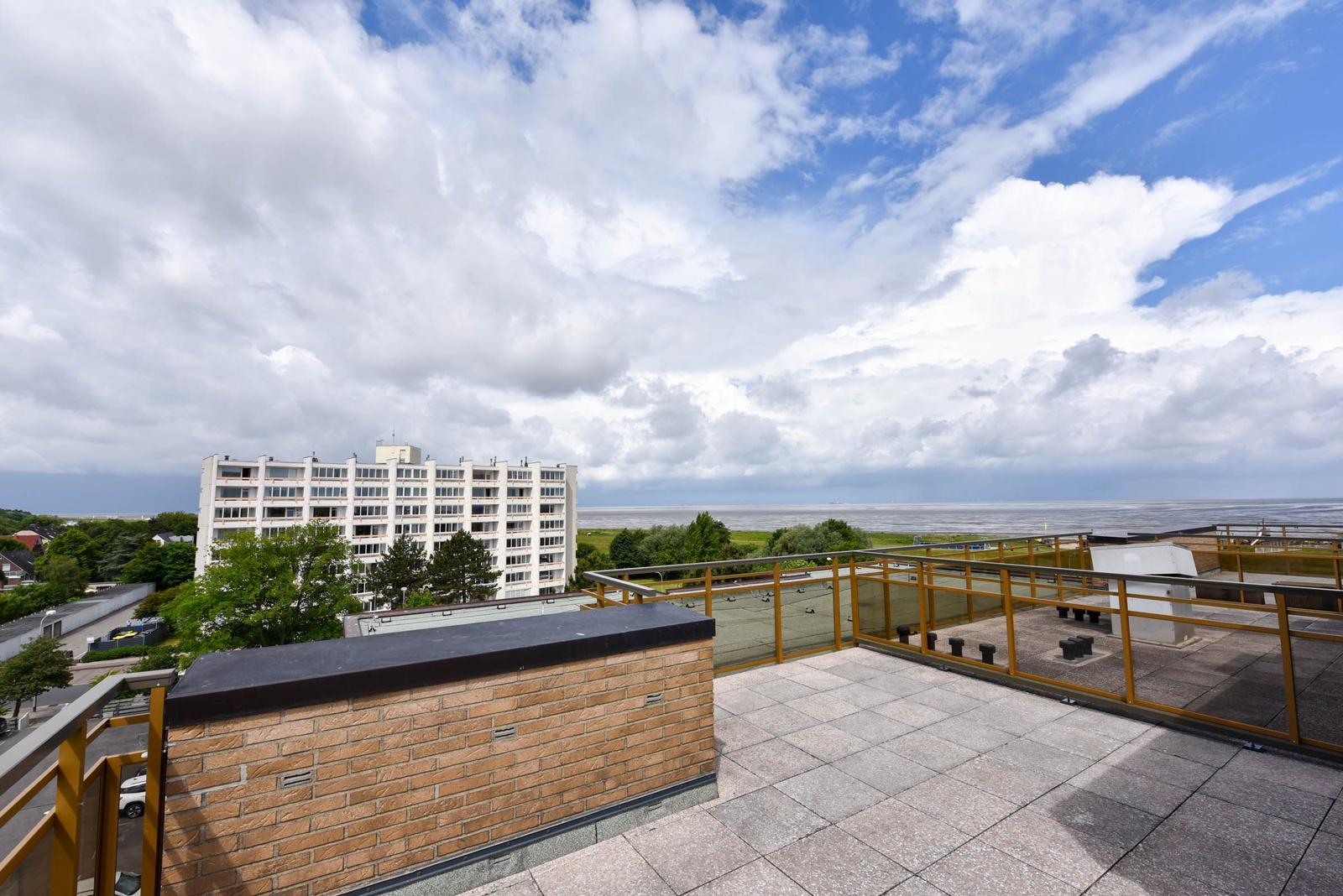Terrasse mit Blick auf Meer und Gebäude unter bewölktem Himmel.