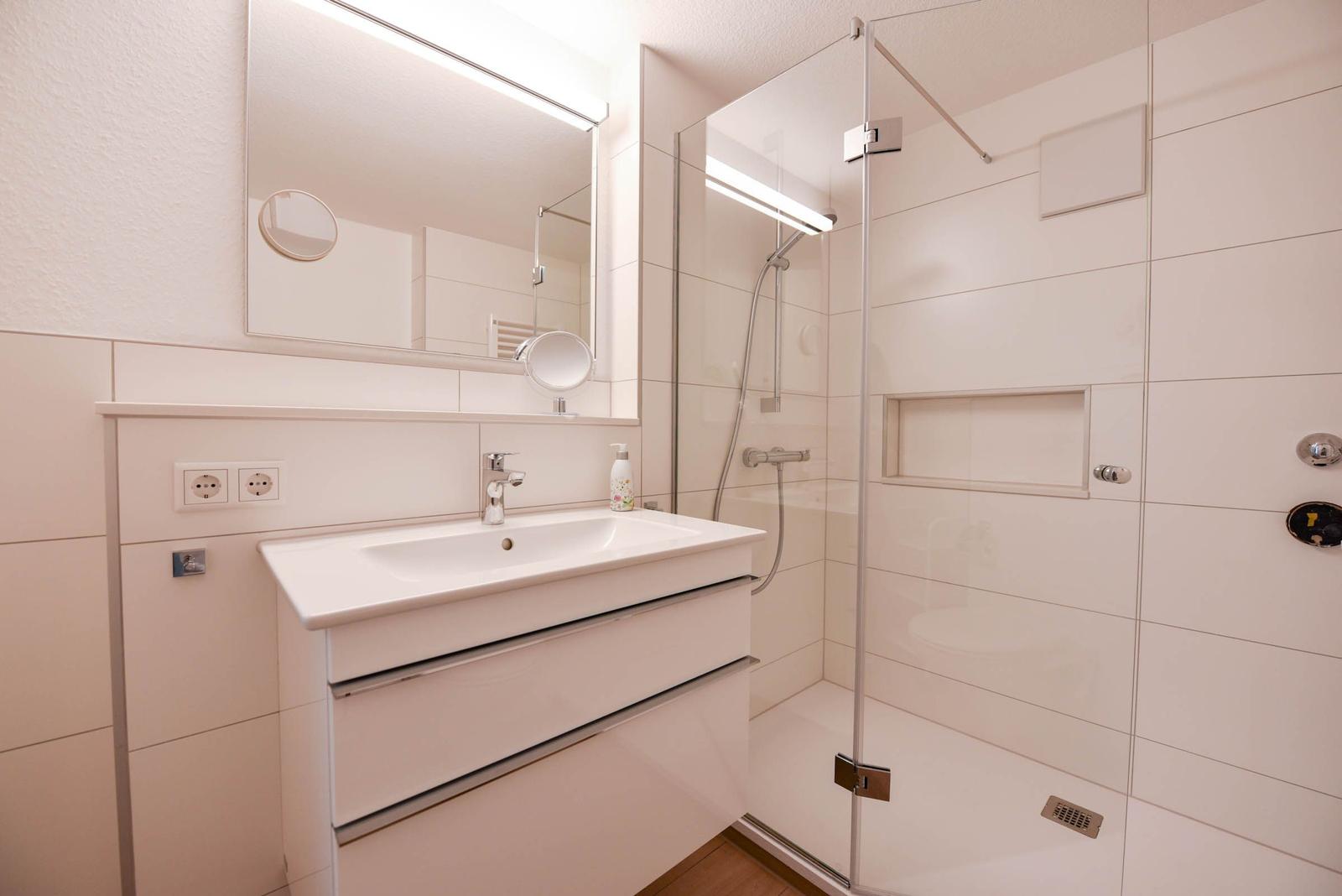 Badezimmer mit Dusche, Waschbecken und Spiegel.