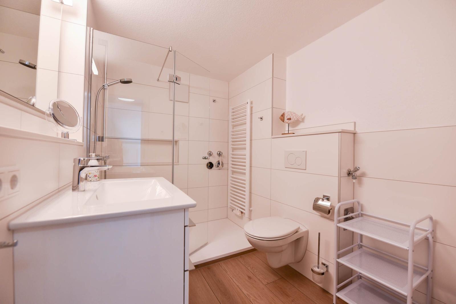 Badezimmer mit Dusche, Waschbecken und Toilette. Holzfußboden und weiße Fliesen.