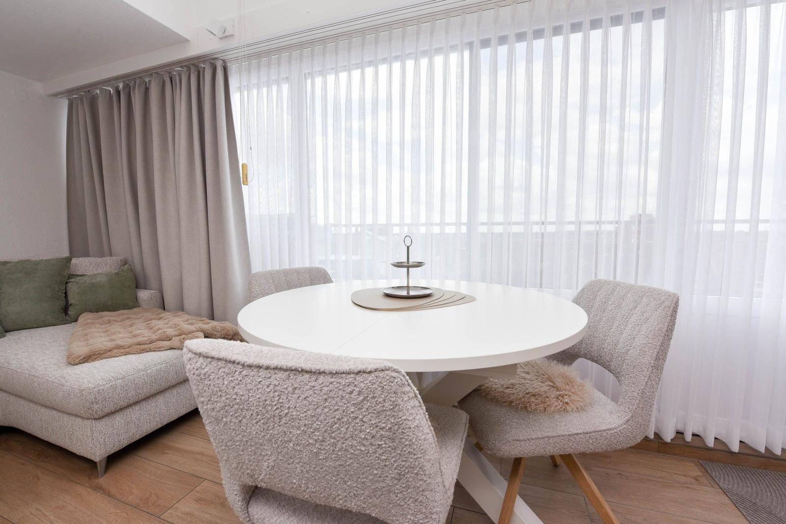 Rundtisch mit Stühlen vor Fenster mit Vorhängen und Sofa.