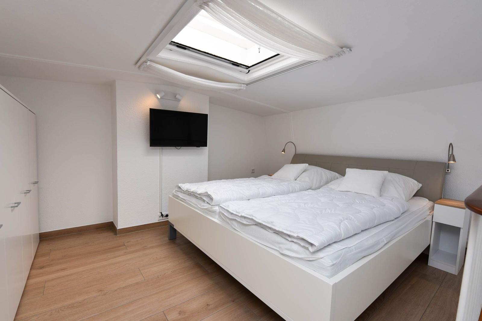 Schlafzimmer mit Doppelbett, TV und Dachfenster.
