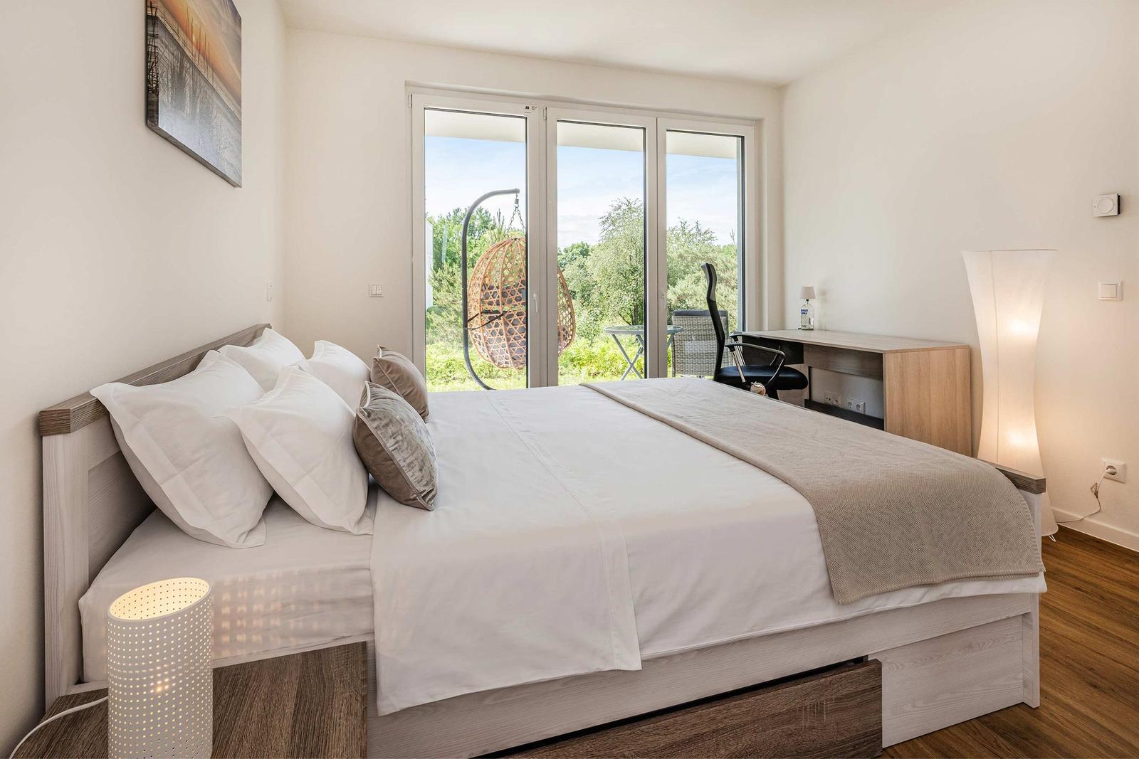 Schlafzimmer mit Bett, Schreibtisch und Balkonansicht
