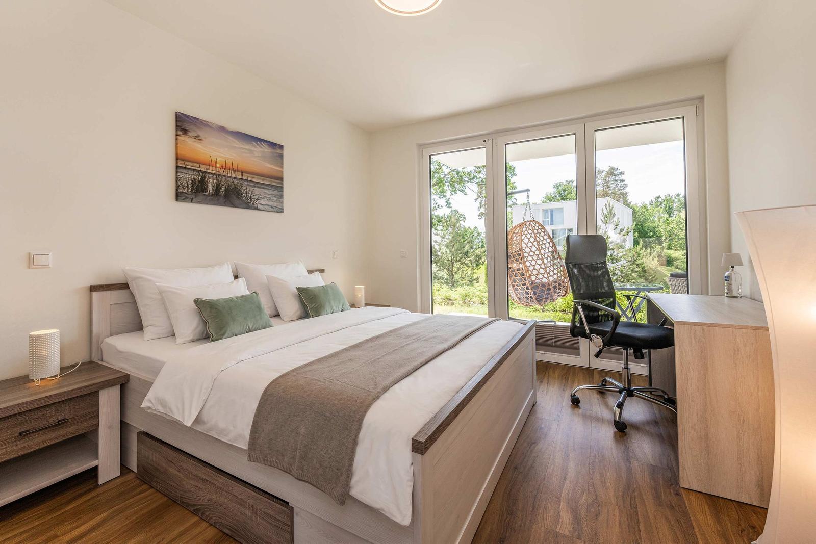 Schlafzimmer mit Doppelbett, Schreibtisch und Blick auf Balkon mit Hängesessel.