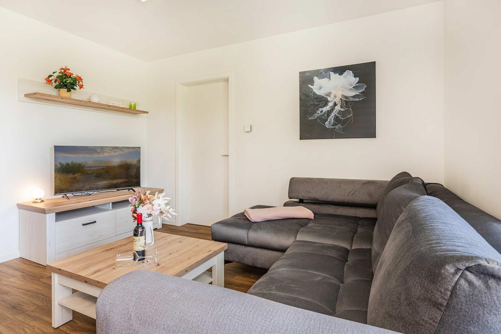 Wohnzimmer mit grauem Sofa, Holztisch und Fernseher an der Wand.
