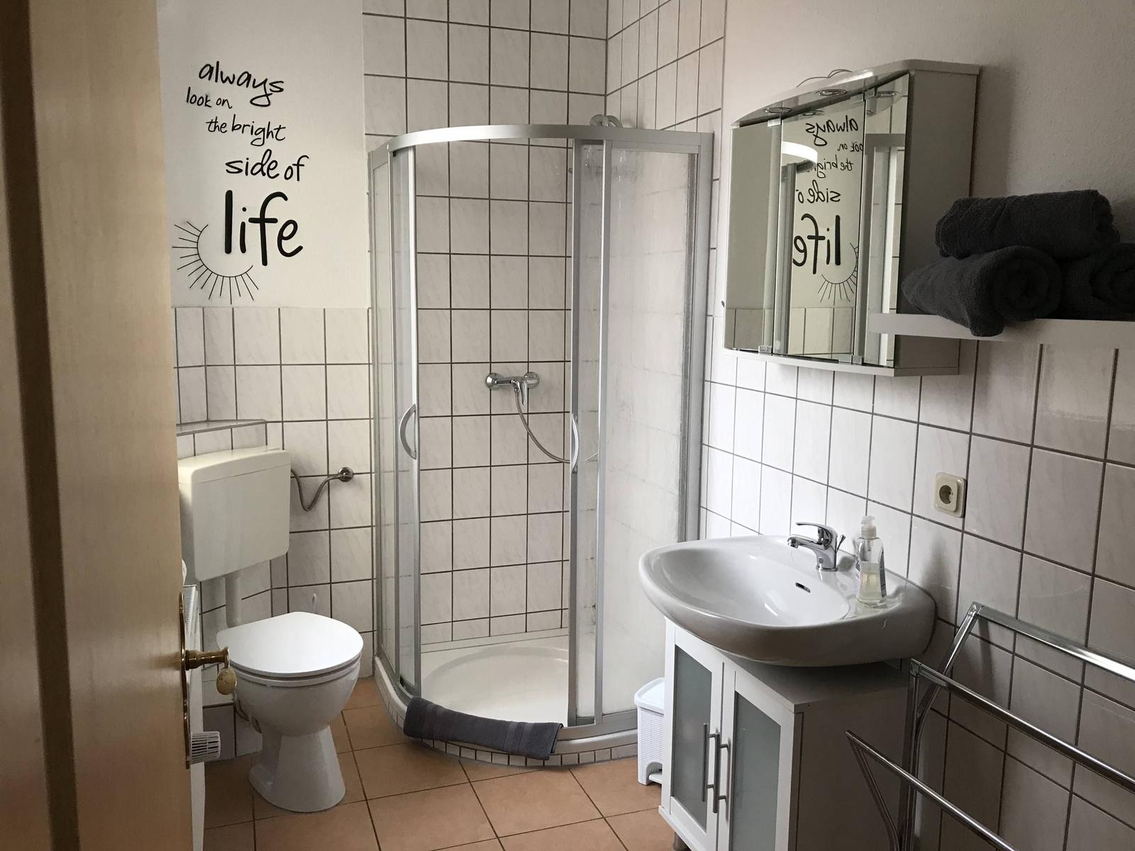 Badezimmer mit Dusche, Waschbecken und Toilette. Wanddekoration mit Motiv.