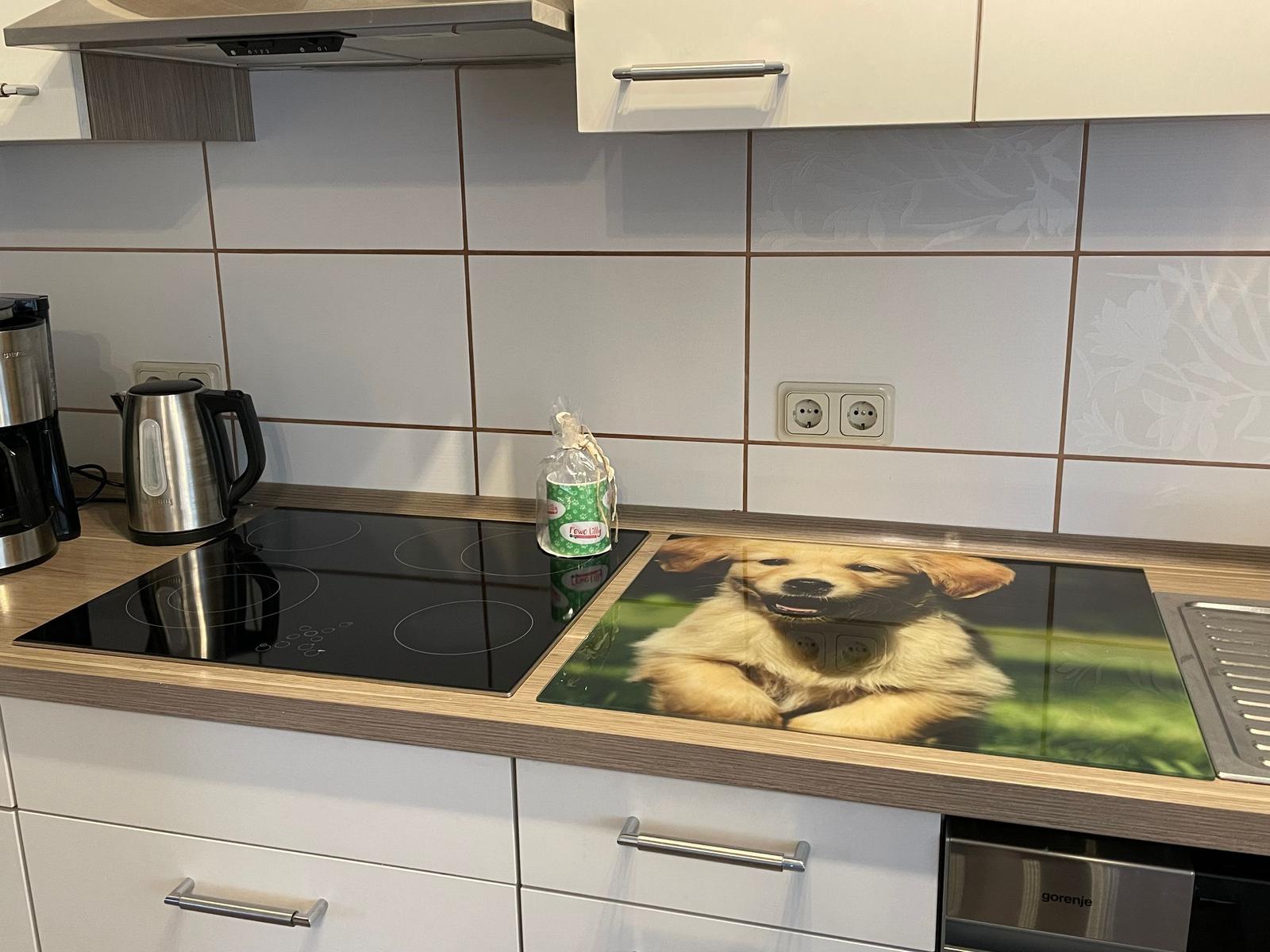 Küche mit Kochfeld, Kaffeemaschine und Hundemotiv auf Arbeitsplatte.