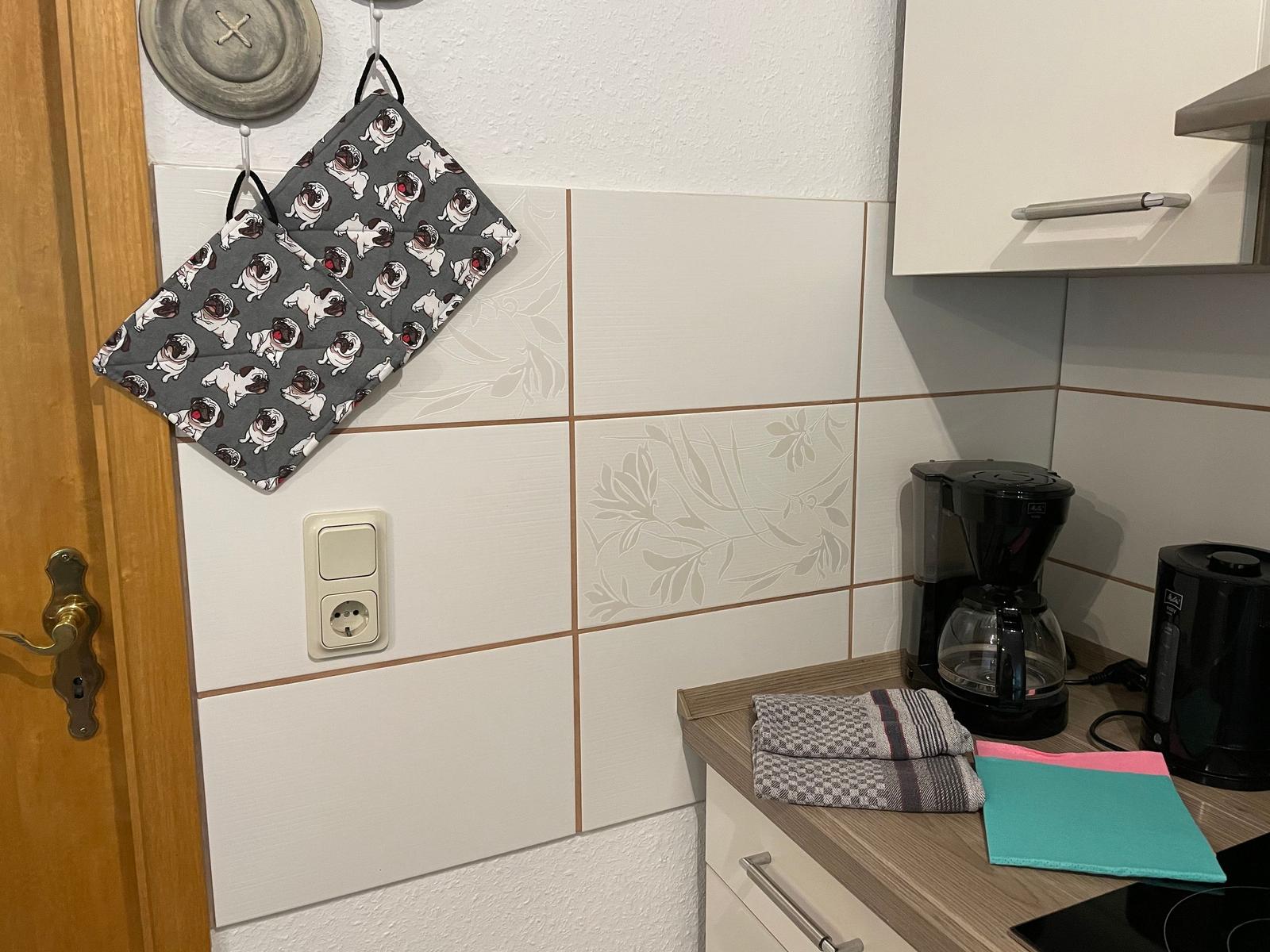 Küchenbereich mit Kaffeemaschine, Handtuch und Pug-Handschuhen an der Wand.