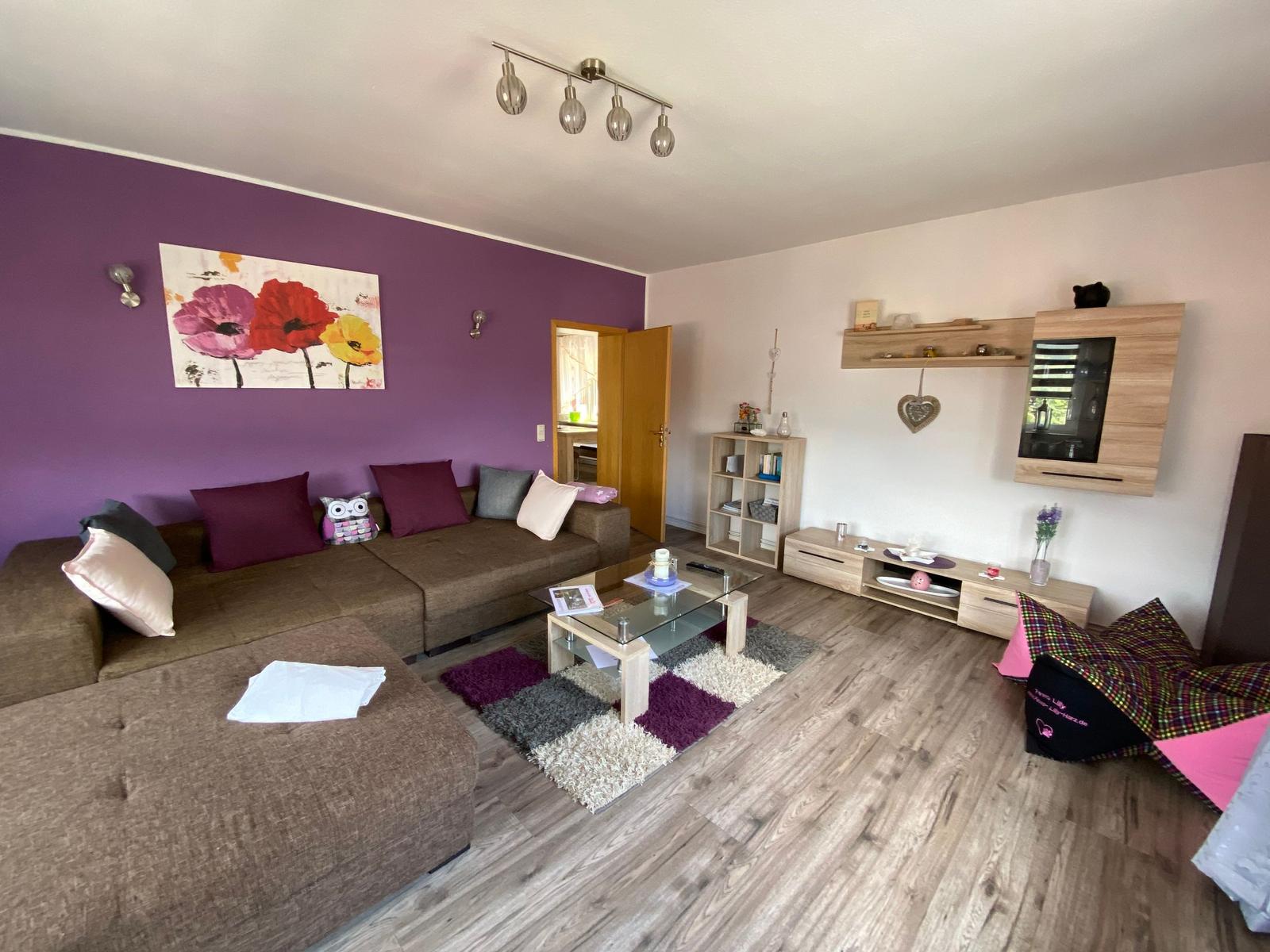 Wohnzimmer mit Sofa, Couchtisch und Wandbild an lila Wand.