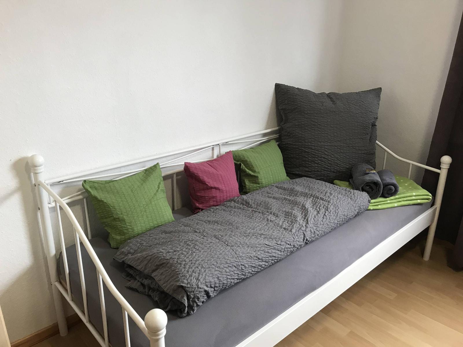 Ein Bett mit grauer Bettwäsche, grünen und rosa Kissen sowie gefalteten Handtüchern.