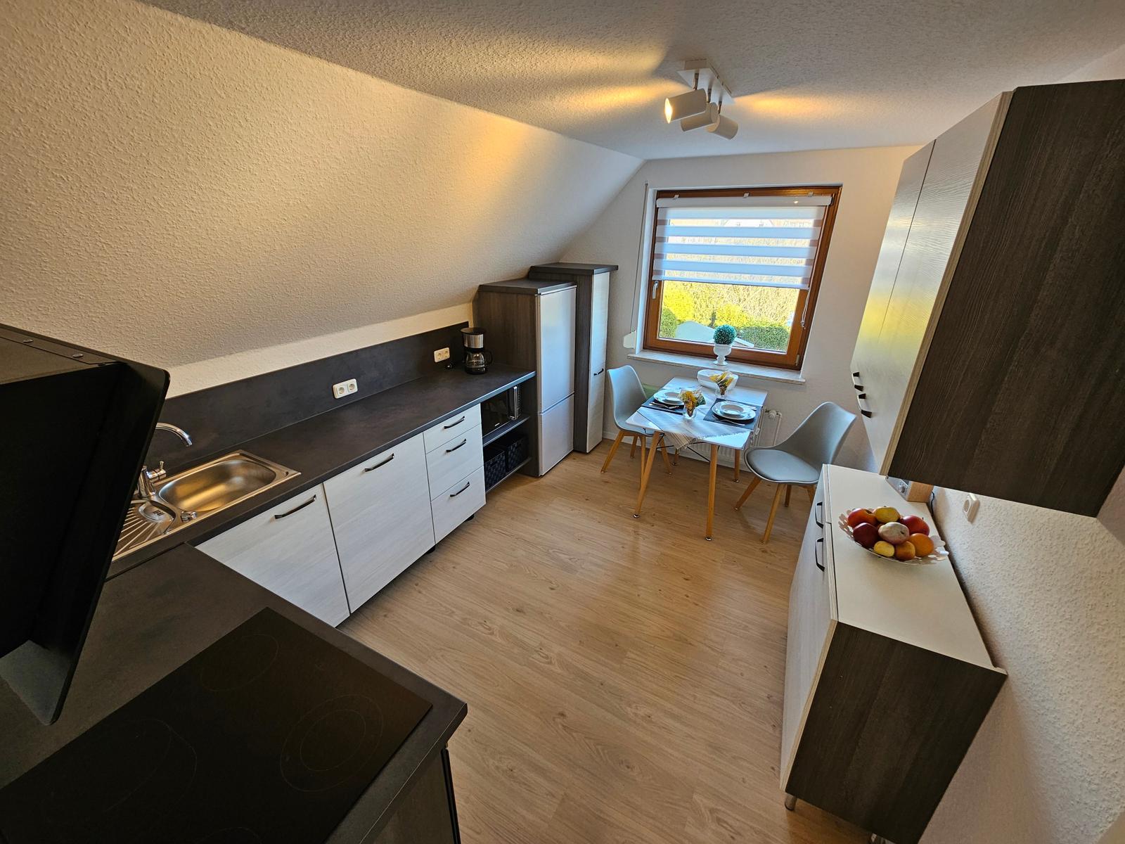Küche mit Essbereich, Fenster, Holzboden und Küchenschränken.
