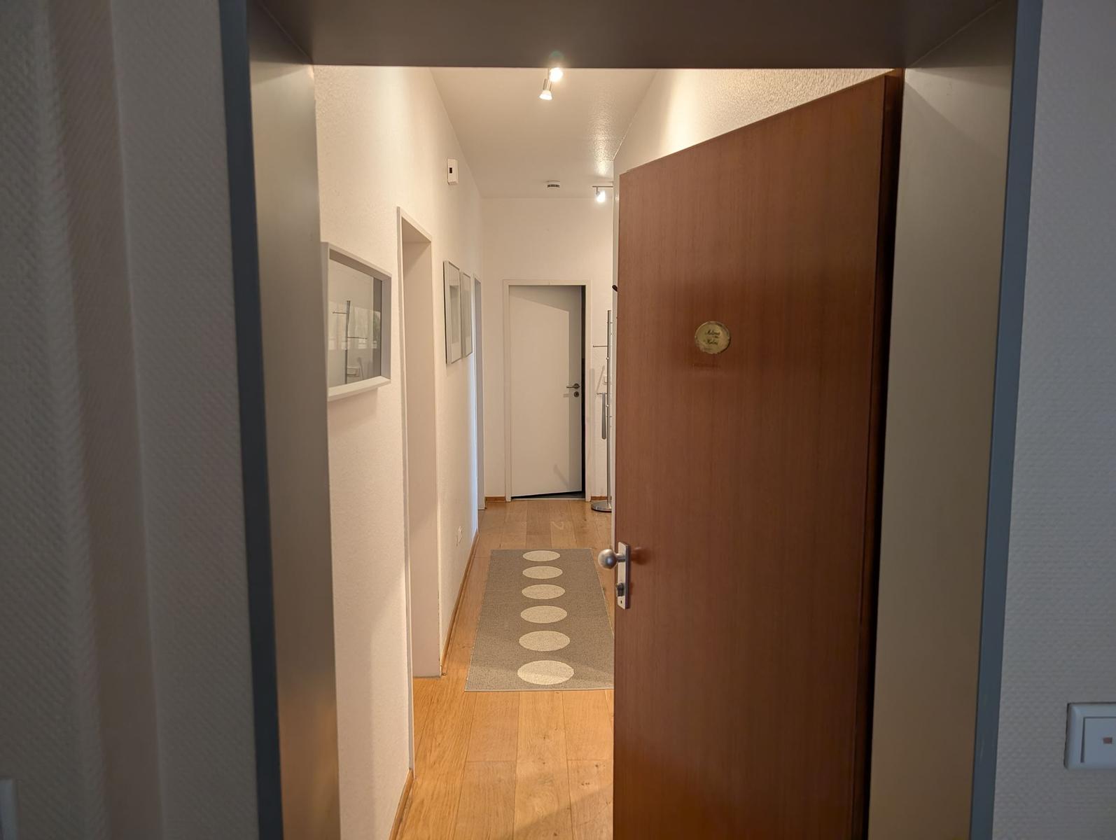 Flur mit Holzboden, Teppich und Türen. Wandbilder und Deckenleuchten sichtbar.
