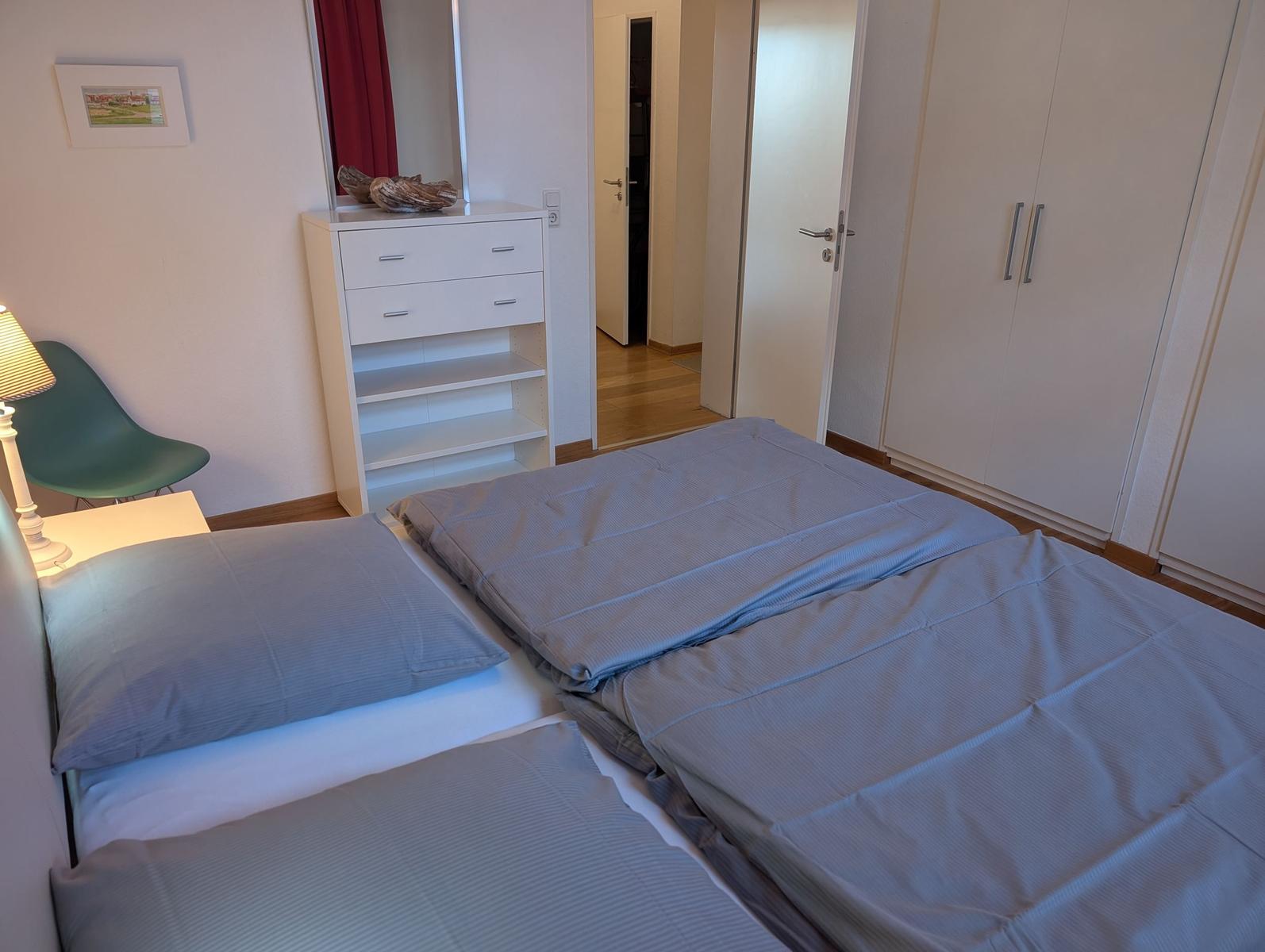 Schlafzimmer mit Bett, Schrank und Nachttisch. Hintergrund: Flur und Kleiderschrank.
