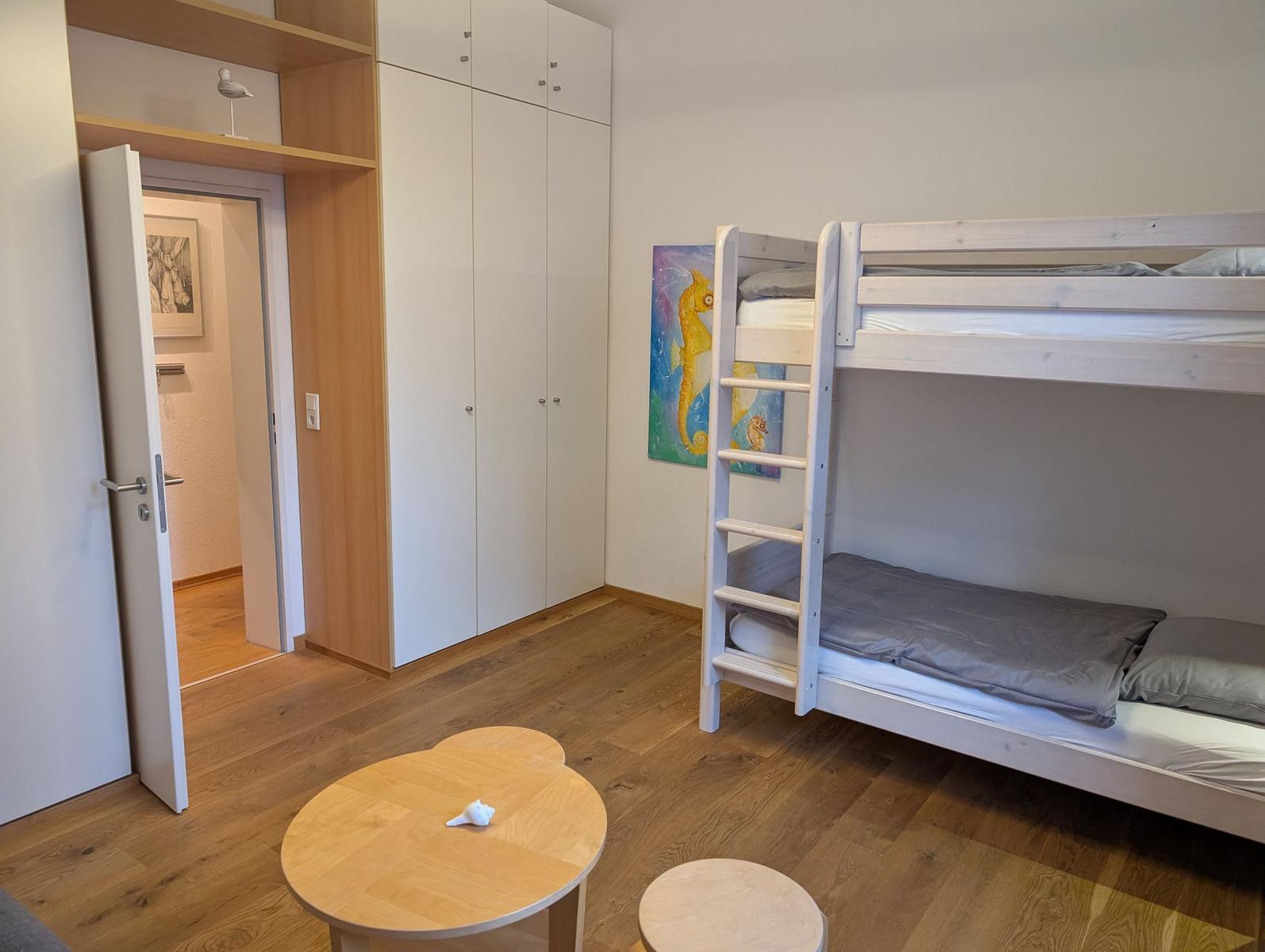 Zimmer mit Doppelstockbett, Kleiderschrank und runden Tischen.