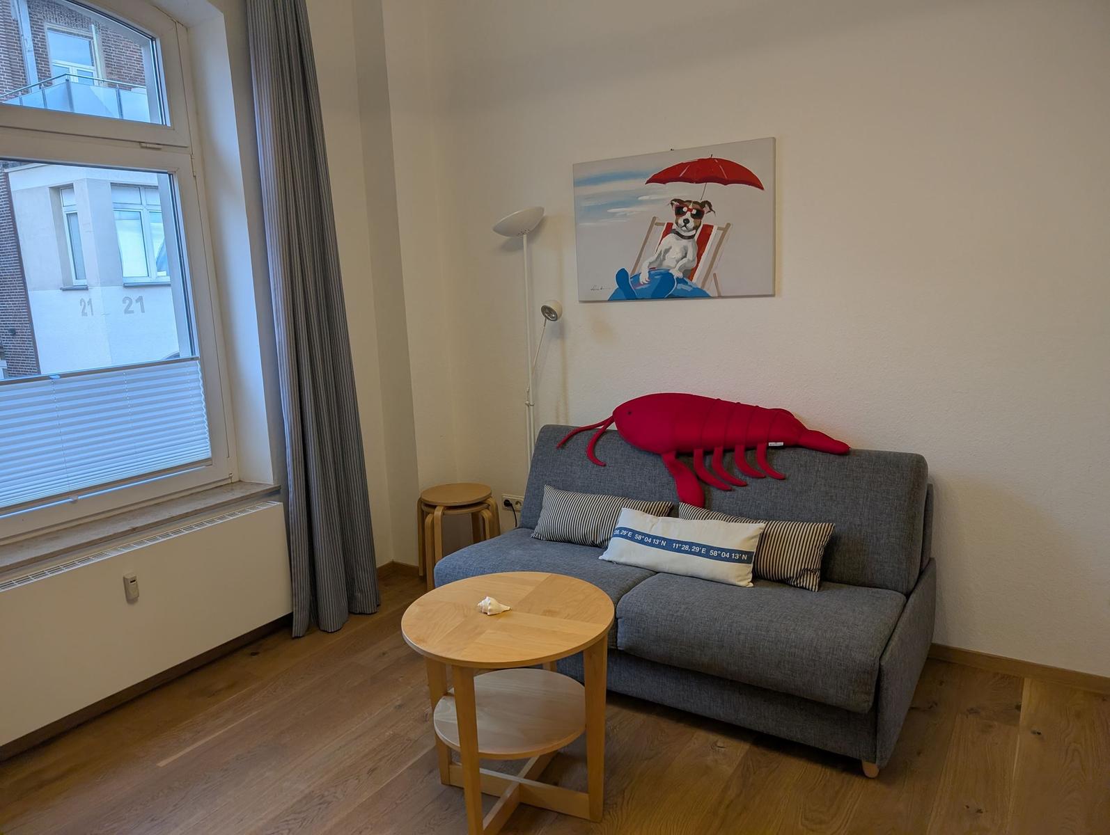 Grauer Sofa mit rotem Garnelenkissen, runder Tisch und Wandbild mit Hund.
