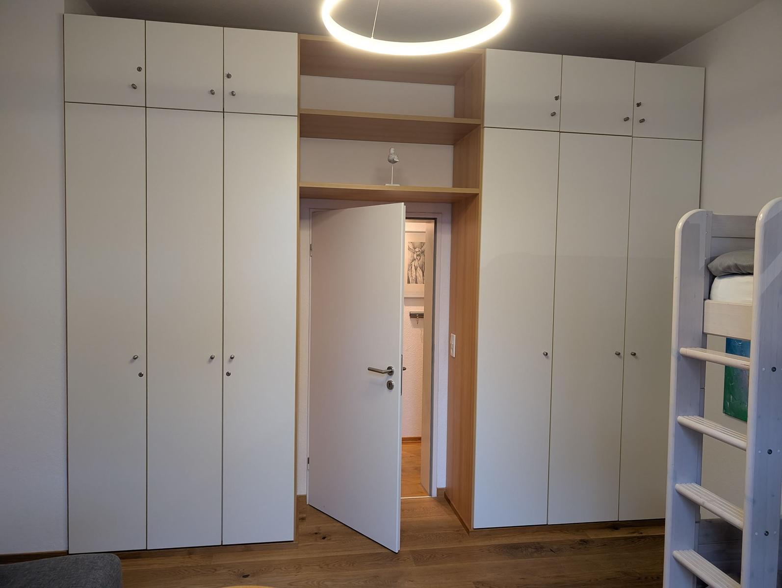 Schlafzimmer mit weißen Schränken, offener Tür und Holzboden.