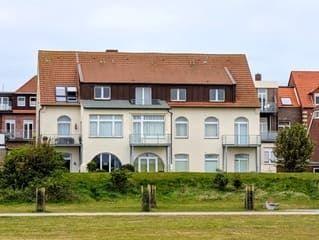Ein zweistöckiges Haus mit rotem Dach und weißen Fenstern steht auf einer grünen Wiese.