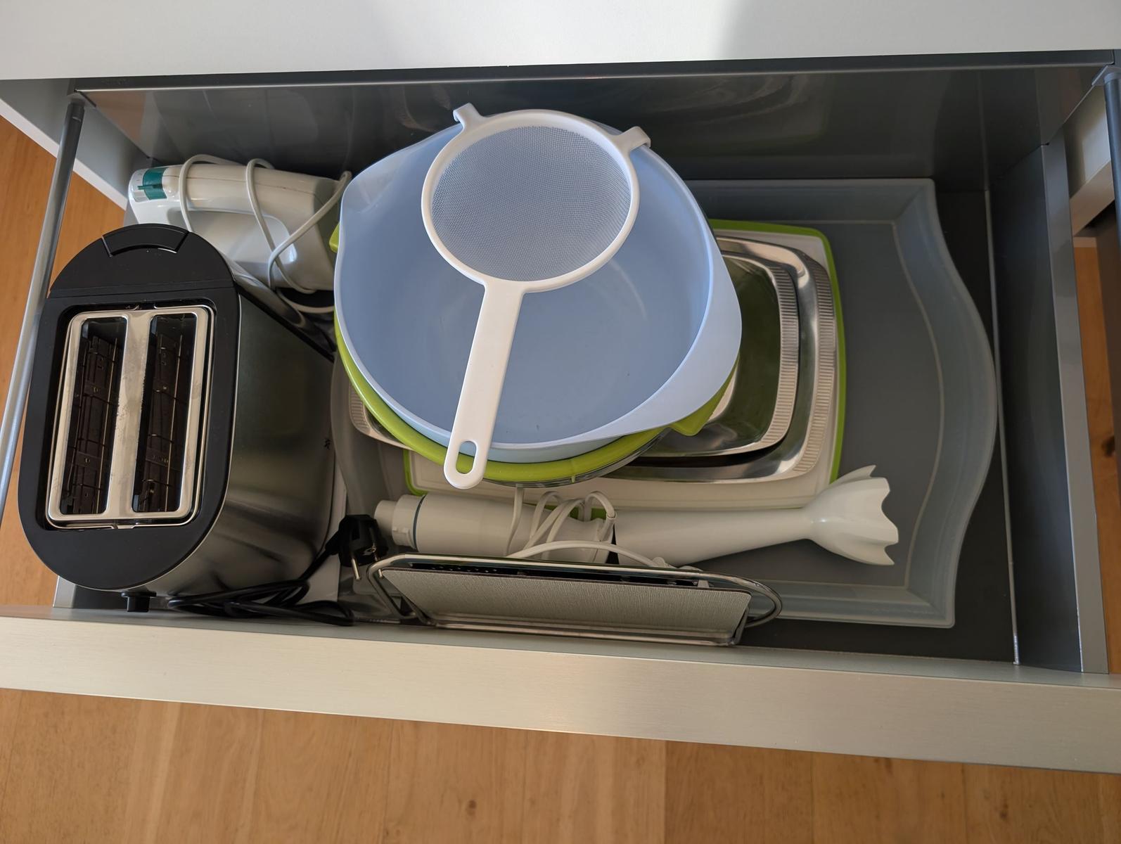 Küchenzeile mit Toaster, Sieb und Küchenutensilien im Schrank.