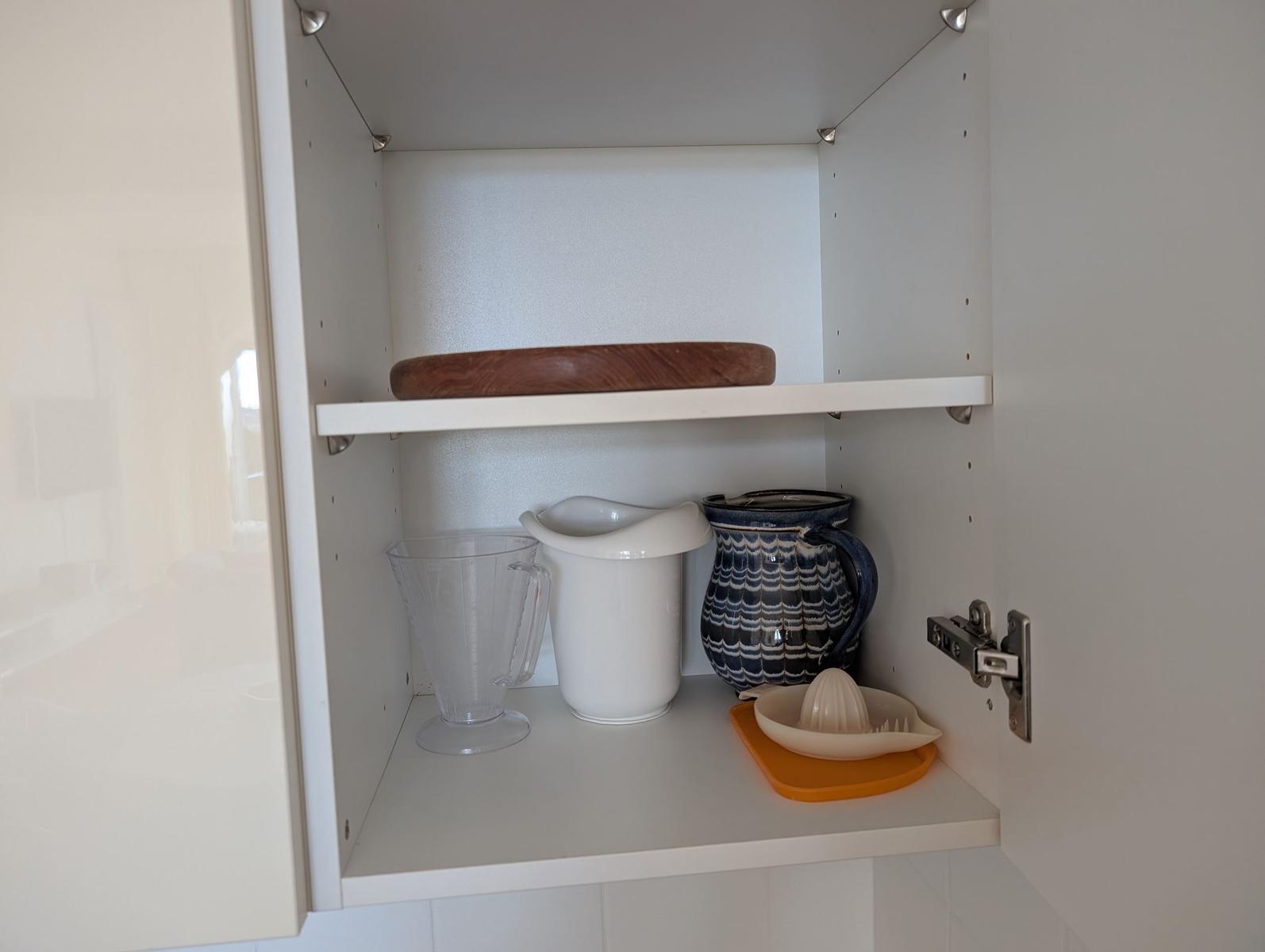 Küchenschrank mit Holzschale, Wasserkaraffe, Zitruspresse und Keramikkrug.