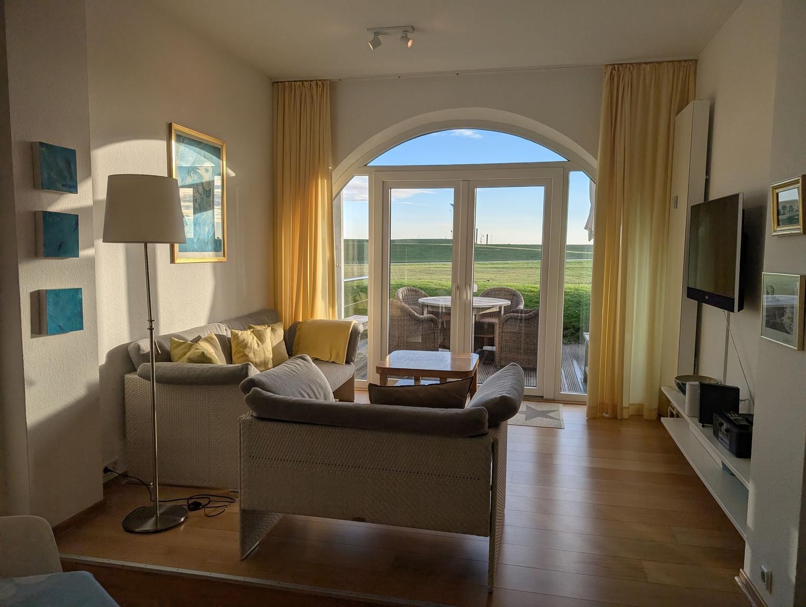 Wohnzimmer mit Sitzgruppe, TV und Blick auf Terrasse mit Garten.