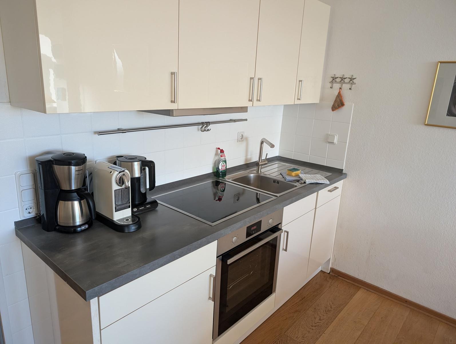 Küche mit Arbeitsplatte, Spüle, Herd und Backofen. Weiße Schränke und Holzboden.