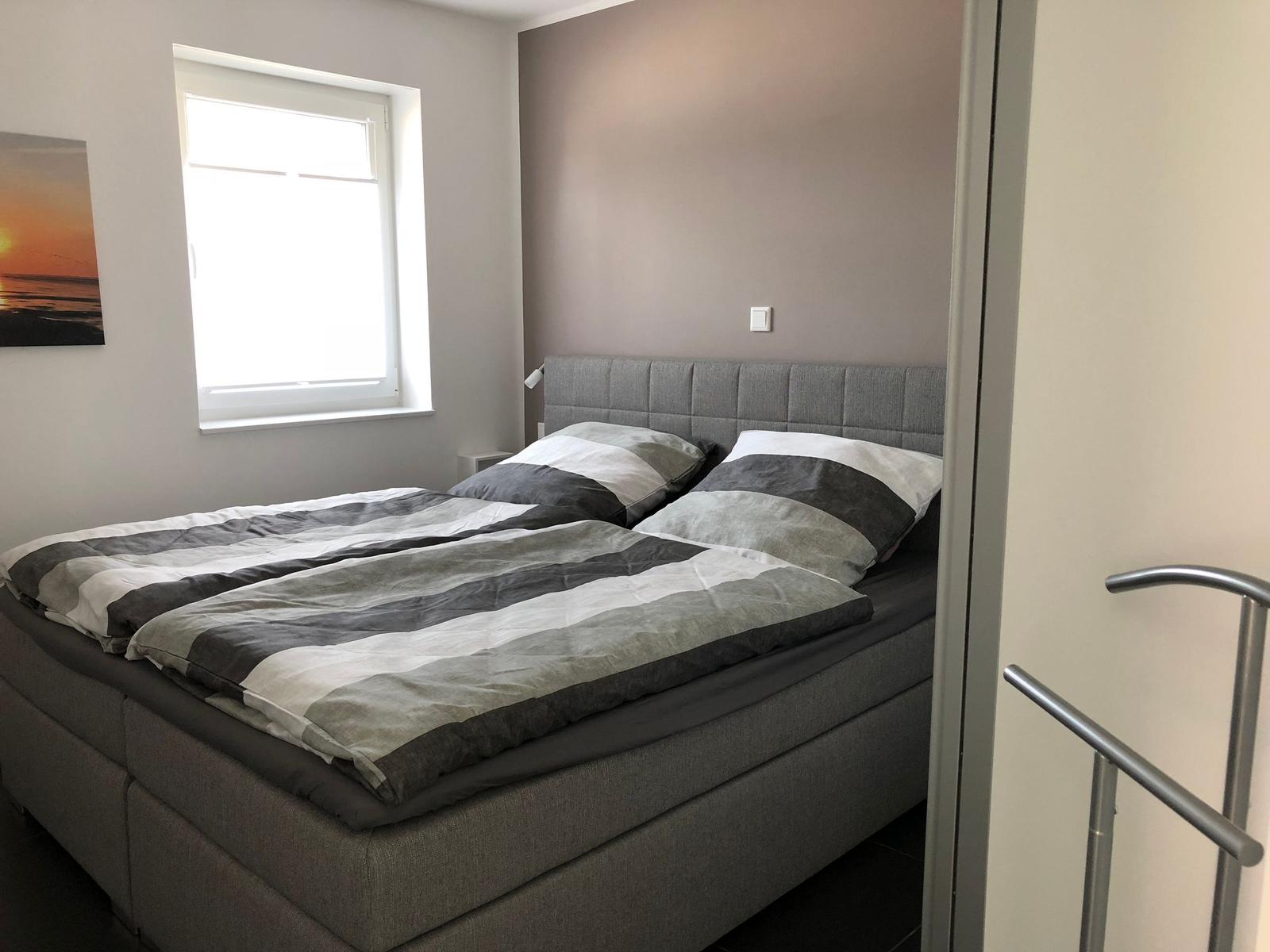 Ein Schlafzimmer mit Doppelbett, Fenster und Wandbild.