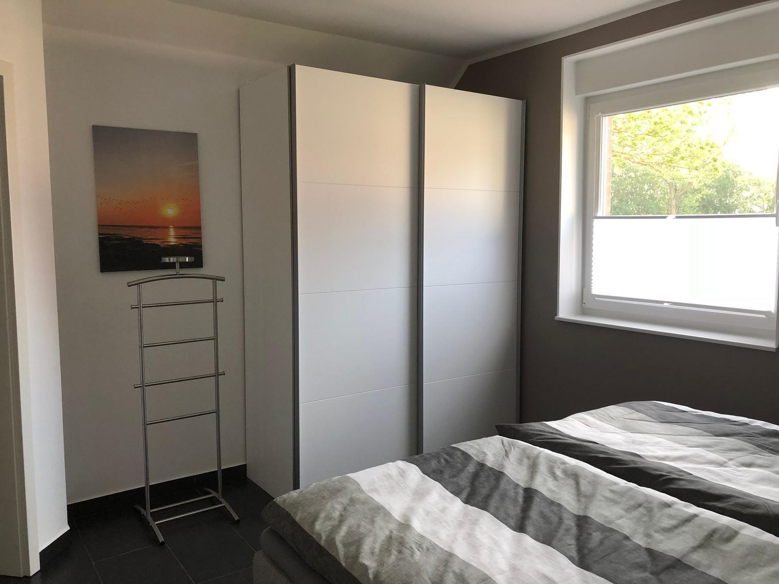 Schlafzimmer mit Bett, Kleiderkabinen und Fenster mit Blick auf Bäume.