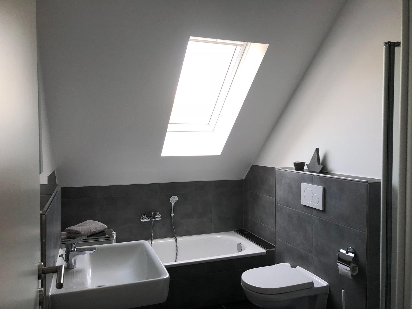 Badezimmer mit Dachfenster, Badewanne, Waschbecken und Toilette.