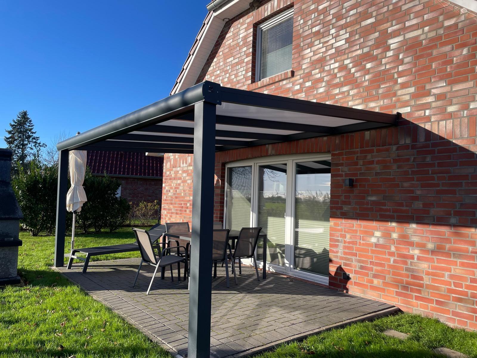 Terrasse mit Sitzgruppe unter Markise neben Haus mit Backsteinwand.