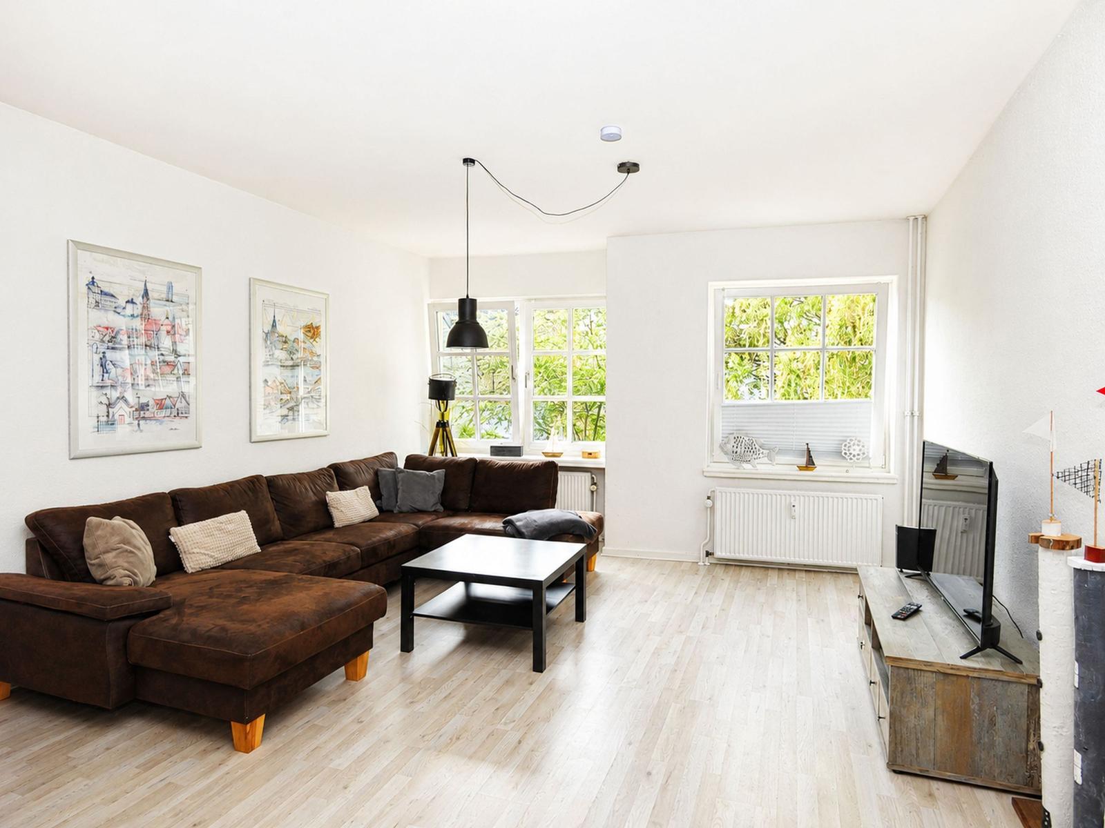 Wohnzimmer mit braunem Sofa, Holzboden und Fenstern zum Garten