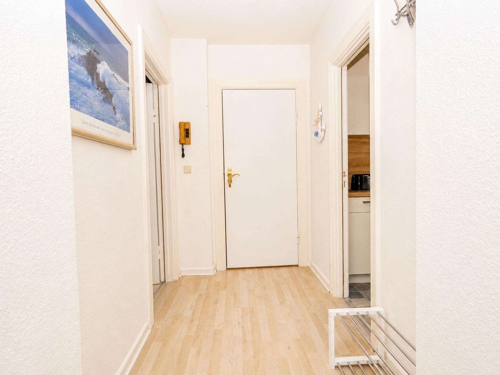 Flur mit Holzboden, weißen Wänden und Tür. An der Wand hängt ein Bild.