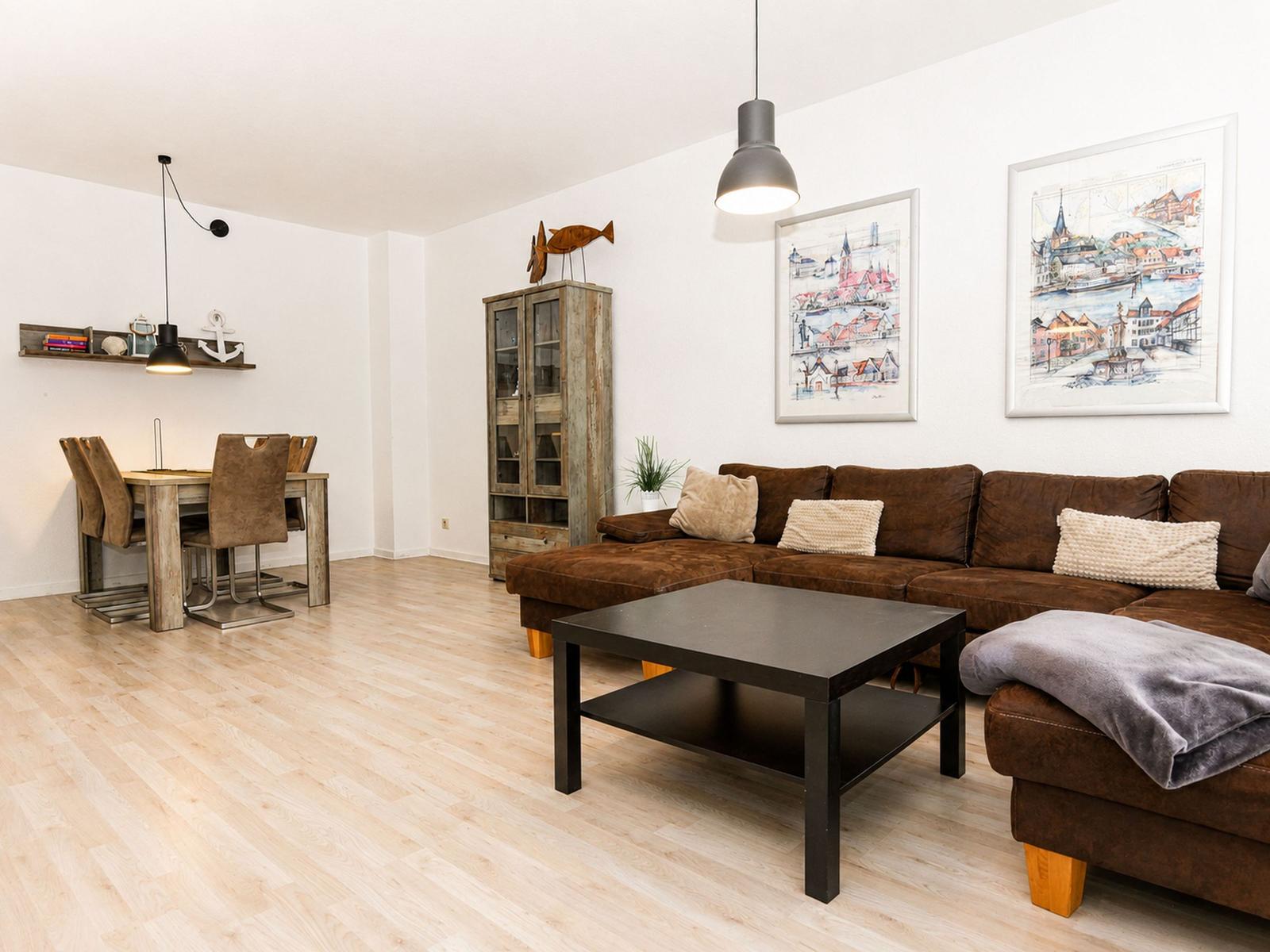 Wohn- und Essbereich mit braunem Sofa, Holzboden und Wandbildern.