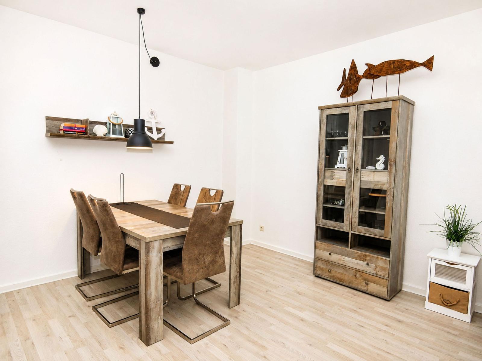 Esszimmer mit Holztisch, Stühlen und Sideboard. Wandregal und Dekoration sichtbar.
