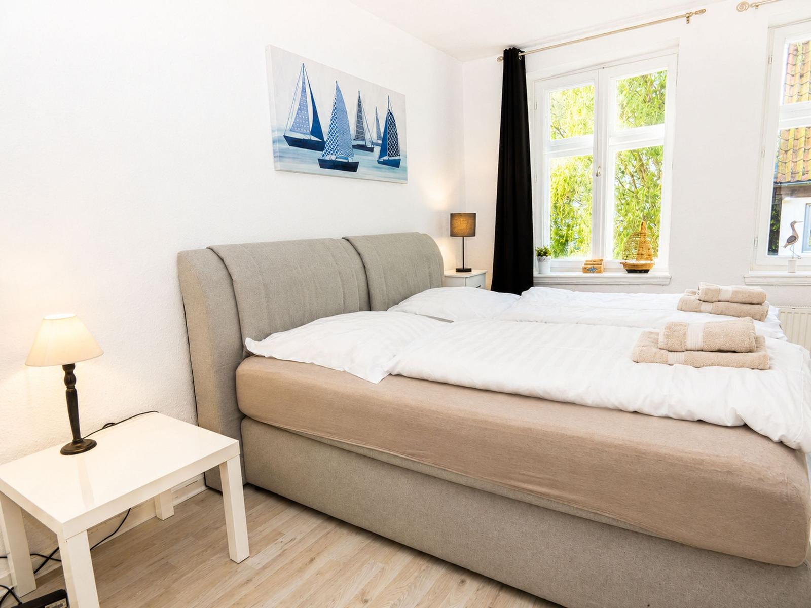 Schlafzimmer mit Doppelbett, Fenster und Wandbild mit Segelbooten.