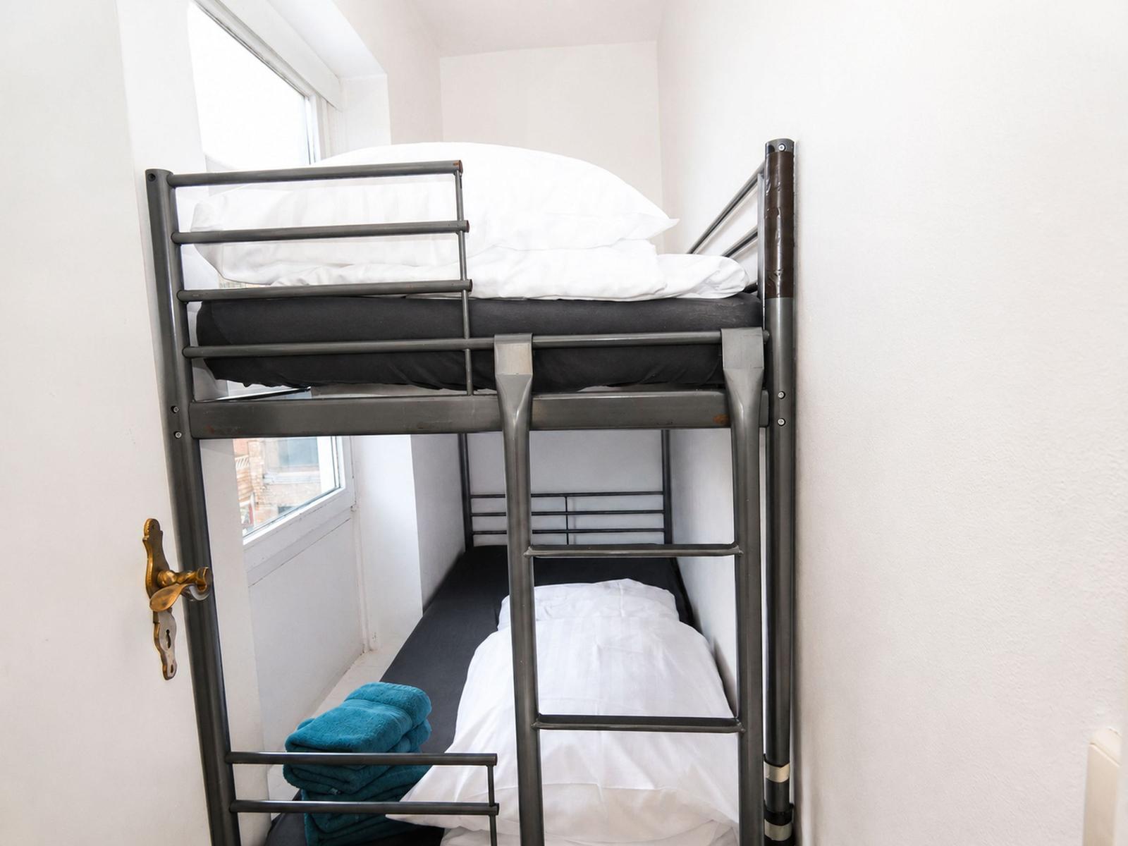 Doppelstockbett mit weißer Bettwäsche und blauen Handtüchern neben einem Fenster.