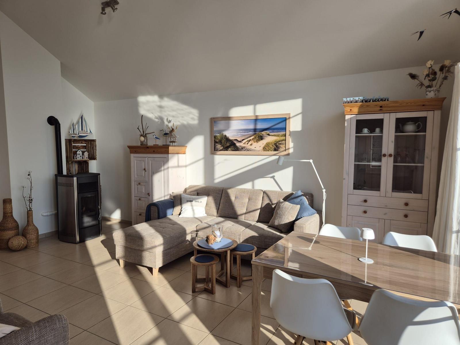 Wohn- und Essbereich mit Sofa, Esstisch und Kaminofen. Wandbild zeigt Strand.