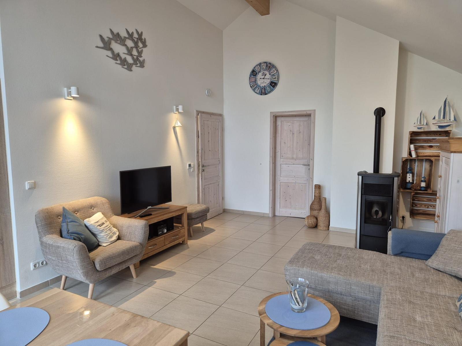 Wohnzimmer mit Sofa, Fernseher und Kaminofen. Holzmöbel und Wanduhr sichtbar.