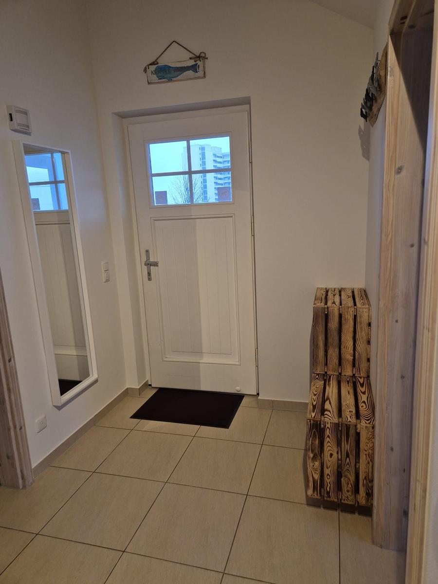 Eingangsbereich mit weißer Tür, Spiegel und Holzregal.