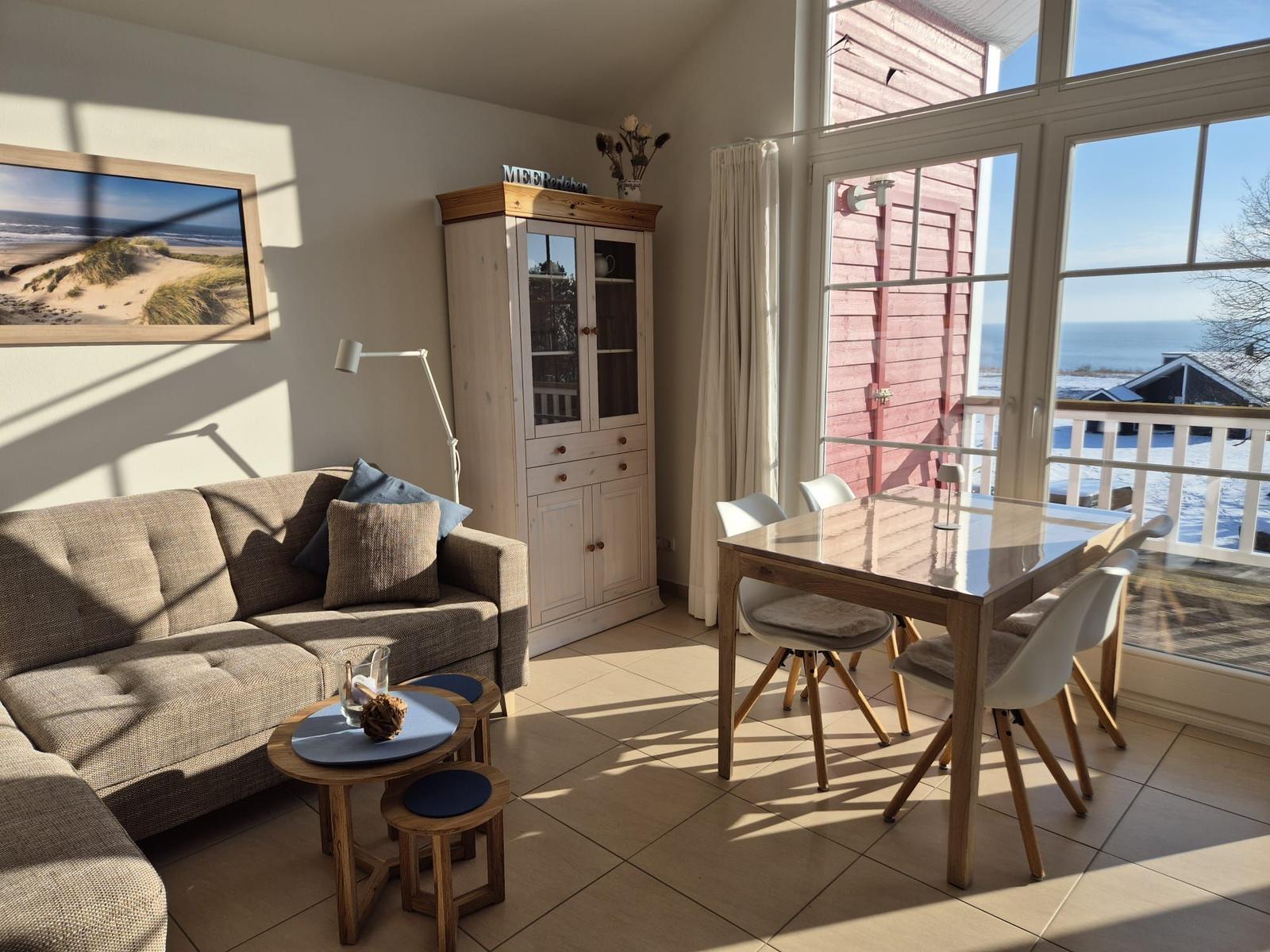 Wohn- und Essbereich mit Blick aufs Meer und Balkon. Möbel aus Holz und Stoff.
