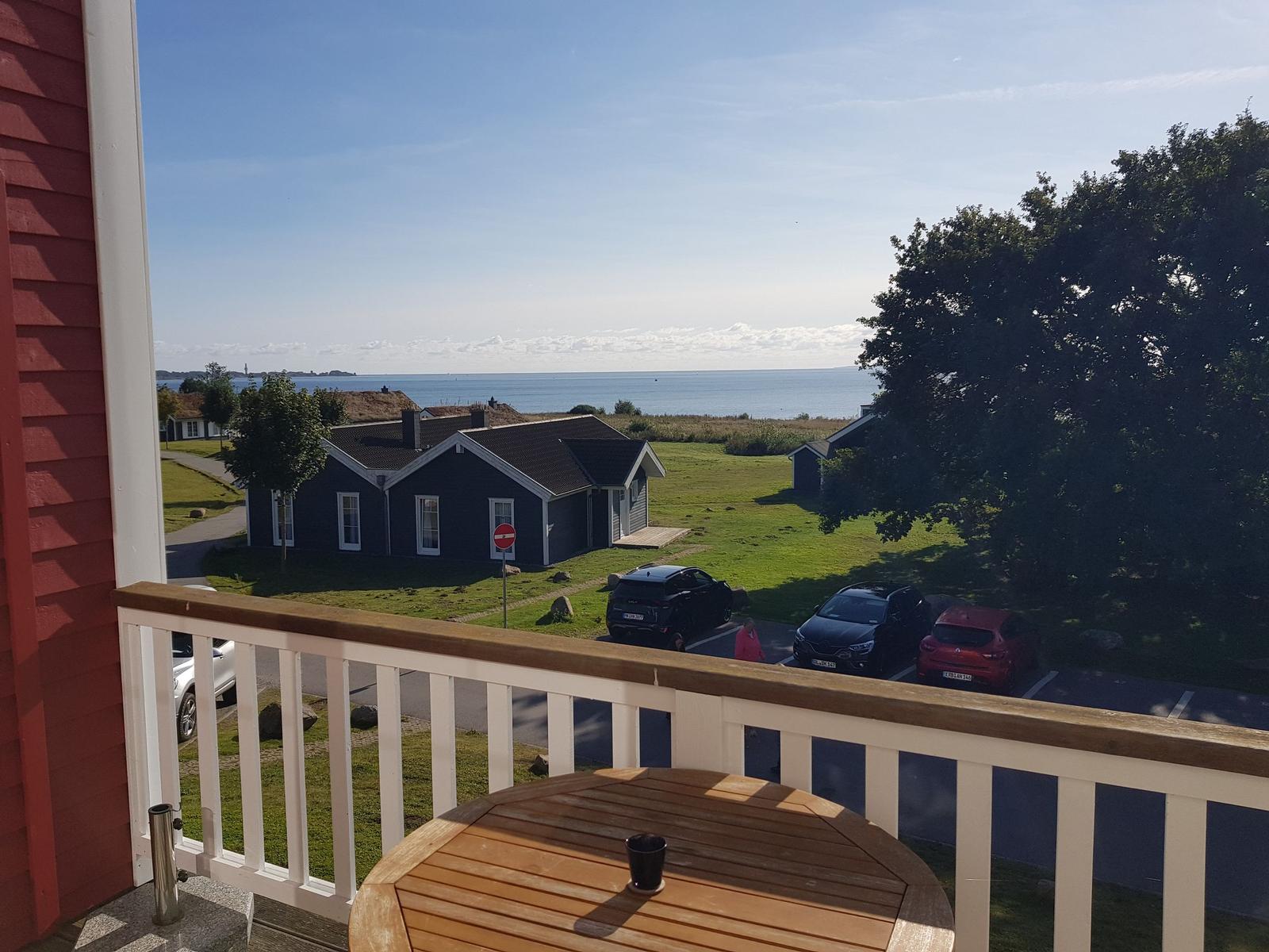 Terrasse mit Tisch, Blick auf Grünfläche, Gebäude und Meer.
