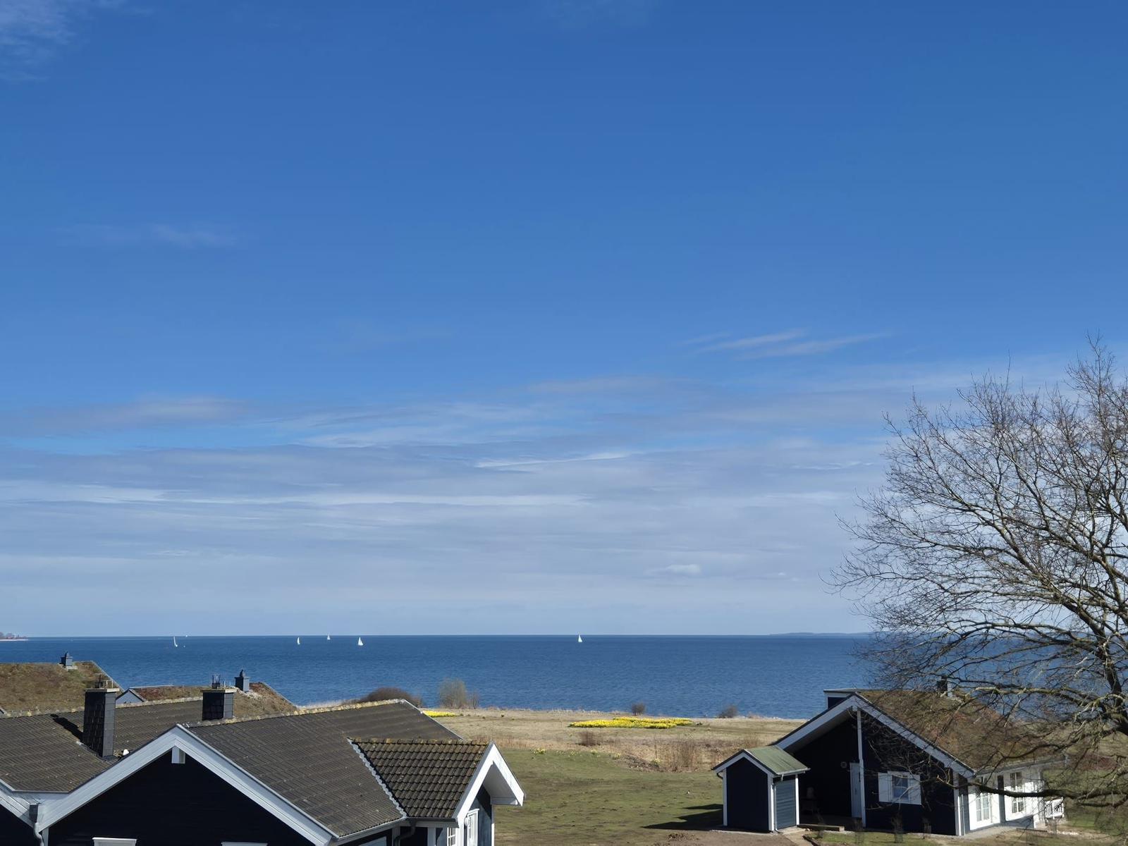 Meeransicht mit Segelbooten und Häusern im Vordergrund unter blauem Himmel.