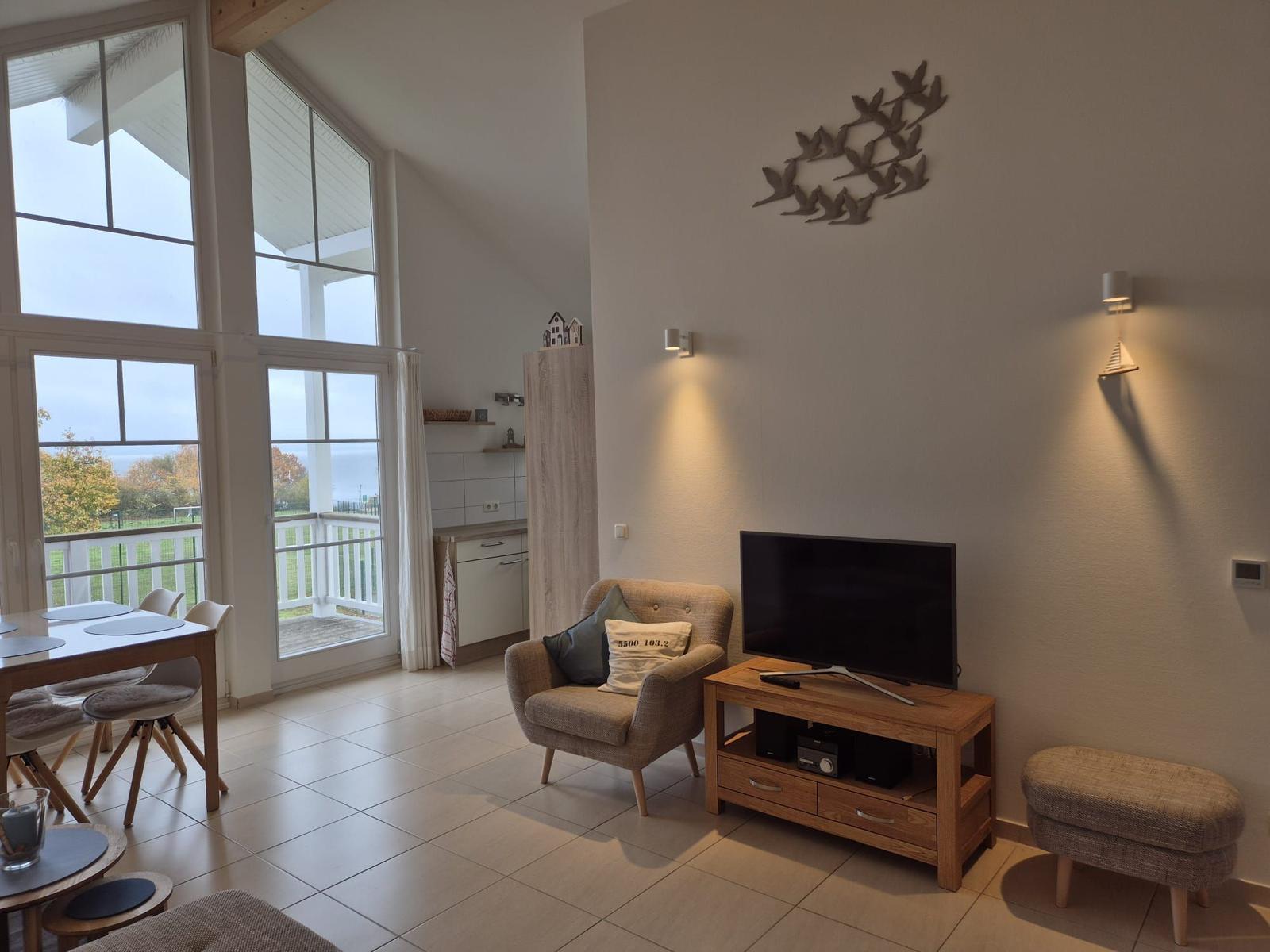 Wohnzimmer mit TV, Sessel und Blick auf Balkon. Wanddekoration und Holzmöbel.