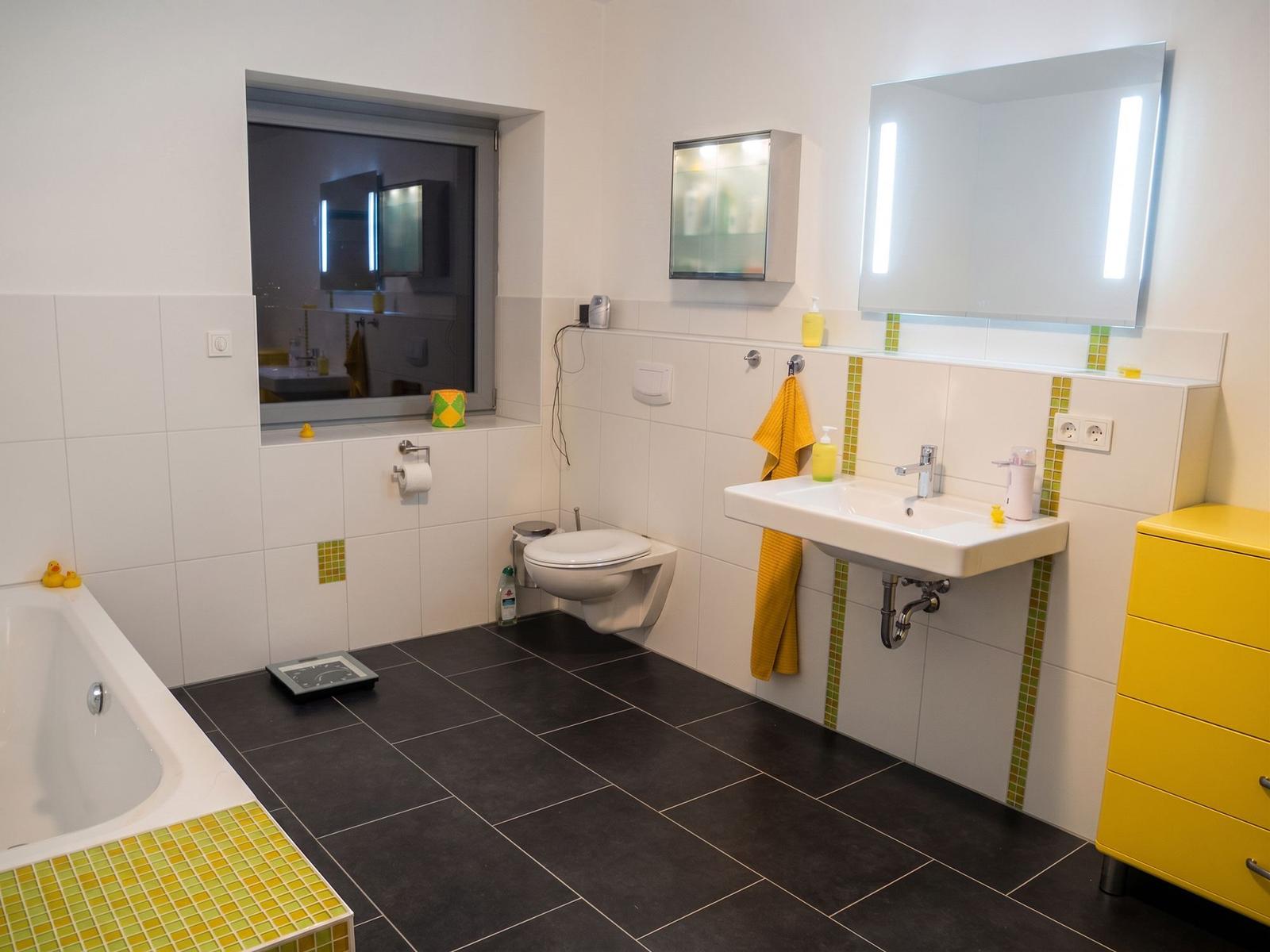 Badezimmer mit Badewanne, Waschbecken, Toilette und gelbem Schrank.