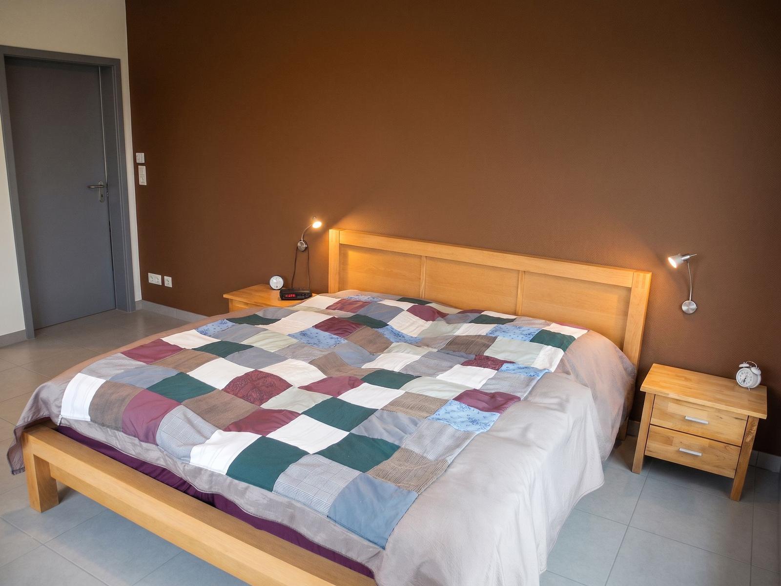 Schlafzimmer mit Holzbett, gemustertem Deckenbezug und Nachttischen mit Lampe.